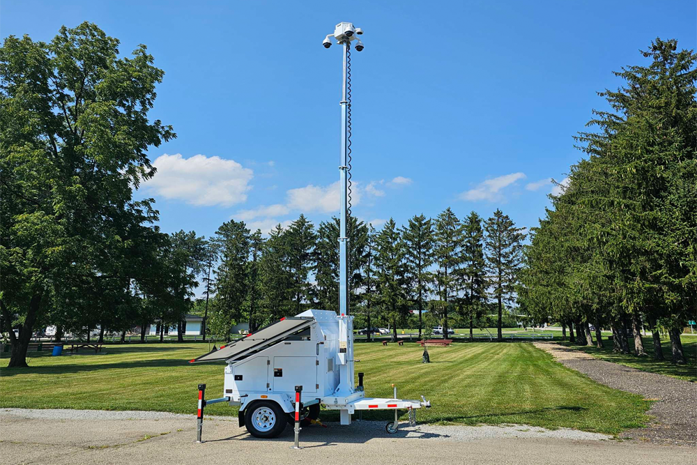 a white surveillance trailer with a light pole and solar panels in the middle of grass